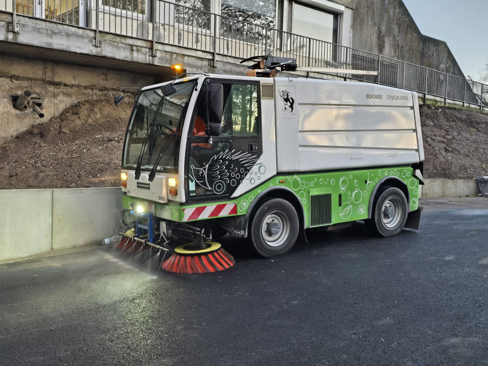 Balayeuse aspiratrice lourde Caron et Fils nettoyant la boue sur l'asphalte à la sortie d'un grand chantier de terrassement dans les Hauts-de-France